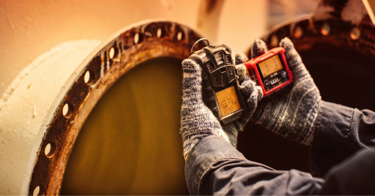 Gas production worker hands holding gas detector sensors in front of a metal tank