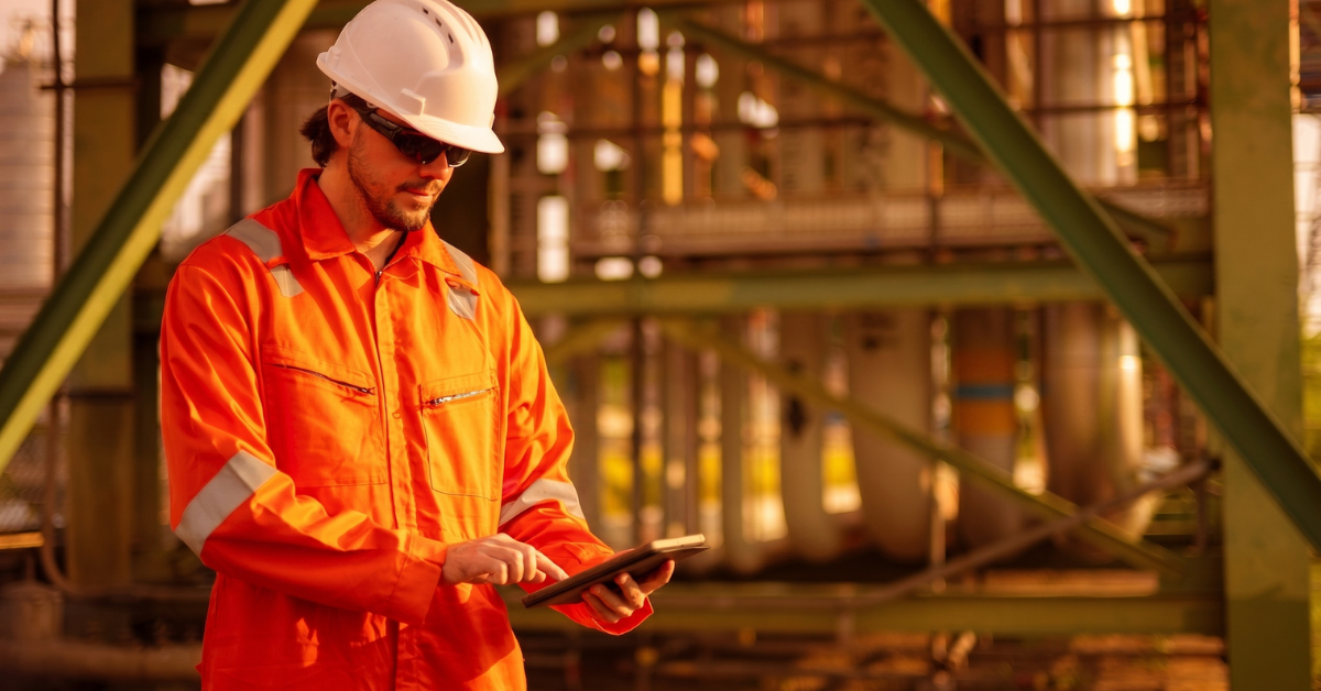 Worker using a tablet and inspecting an oil and gas facility